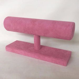 May include: A pink velvet jewellery display stand with a round top for holding bracelets. The stand has a rectangular base.