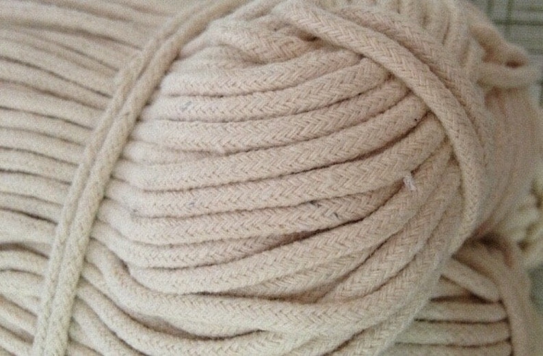May include: A close-up of a large spool of natural-colored cotton rope. The rope is tightly wound and has a braided texture.