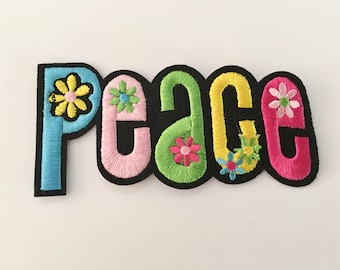 Könnte beinhalten: Ein bunter gestickter Aufnäher mit dem Wort "Peace" im Retro-Stil. Die Buchstaben sind schwarz umrandet und mit bunten Blumen verziert.