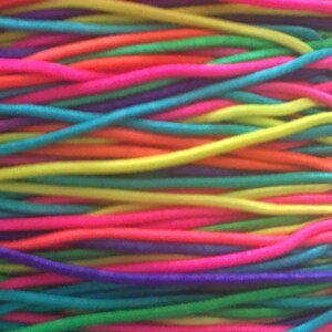Könnte beinhalten: Nahaufnahme eines Bündels bunter Gummibänder. Die Bänder sind in einem Regenbogenmuster angeordnet, wobei jede Farbe deutlich und leuchtend ist.