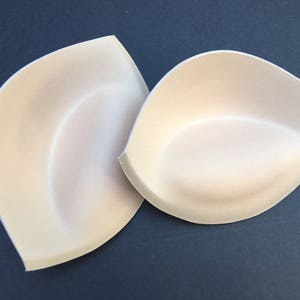 Könnte beinhalten: Zwei beigefarbene Schaumstoffeinlagen für BHs, um dem BH mehr Volumen und Form zu verleihen.