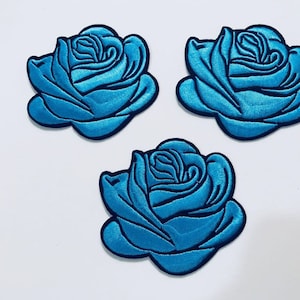 Puede incluir: Tres parches bordados de rosas azules. Las rosas están detalladas con un centro azul claro y contornos azules oscuros.