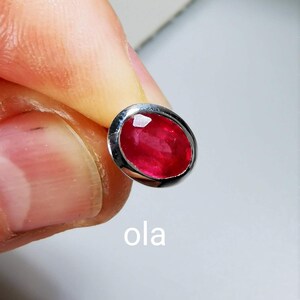 May include: A close-up of a red oval gemstone set in a silver ring. The gemstone is surrounded by a silver bezel setting.
