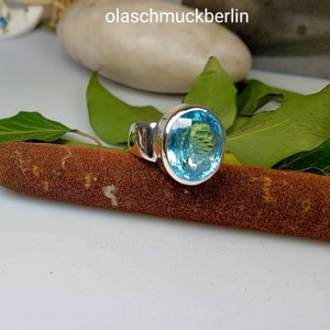 May include: A silver ring with a large, round, light blue gemstone. The ring is set on a brown surface.