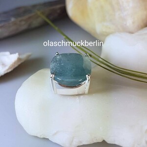 May include: A light blue gemstone set in a silver bezel setting. The gemstone has a slightly cloudy appearance.