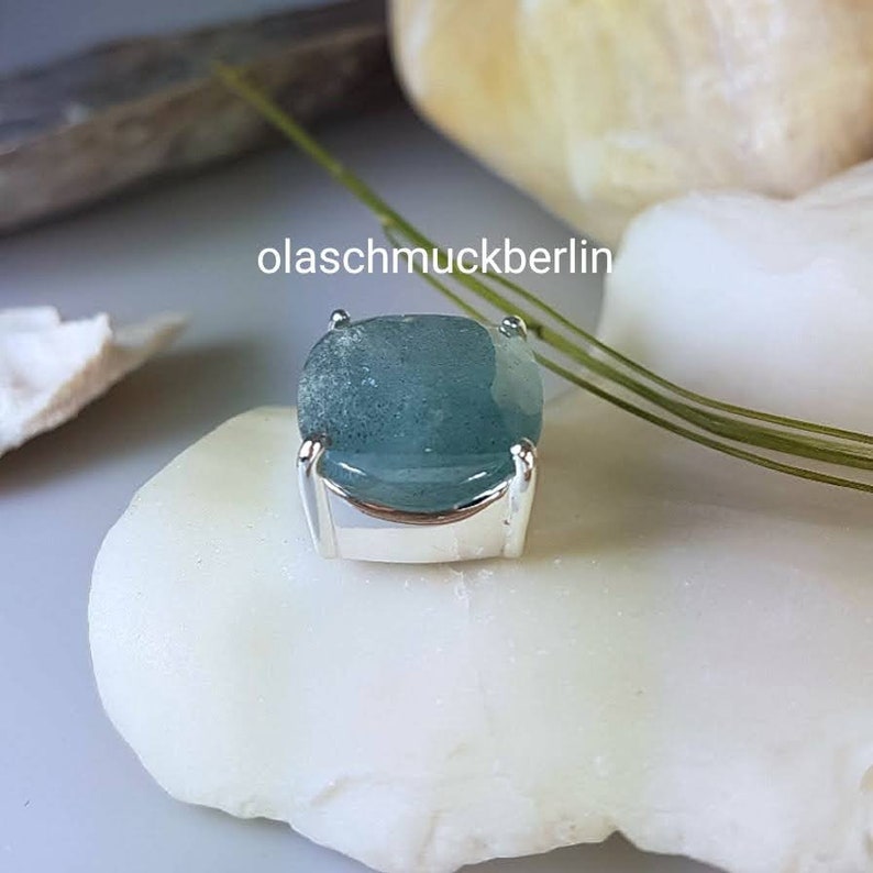 May include: A light blue gemstone set in a silver bezel setting. The gemstone has a slightly cloudy appearance.