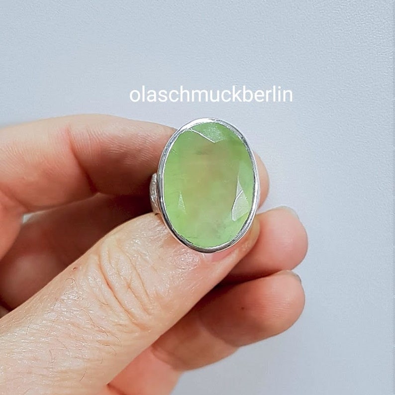 May include: A silver ring with a large, oval-shaped, light green gemstone. The ring is set in a simple, silver band.