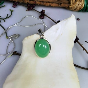 May include: A silver chain necklace with a green oval pendant. The pendant is set in a silver bezel and has a smooth, polished surface.