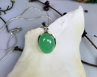 May include: A silver chain necklace with a green oval pendant. The pendant is set in a silver bezel and has a smooth, polished surface.