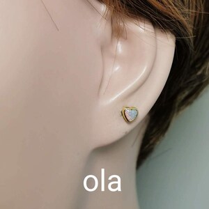 May include: A pair of gold heart-shaped earrings with opal stones. The earrings are shown on a model's ear.