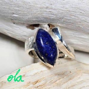 May include: A silver ring with a deep blue lapis lazuli gemstone set in a leaf-shaped design. The ring is textured and has a unique, twisted band.