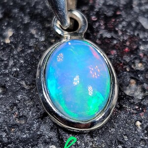 May include: A silver pendant with a light blue opal gemstone. The opal has a green and pink iridescent sheen.