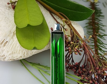 May include: A green crystal pendant with a silver setting. The pendant is rectangular in shape and has a faceted design. The pendant is hanging from a silver chain.