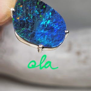 May include: A dark blue opal gemstone set in a silver pendant setting. The opal has a black base with green and blue flashes of color.