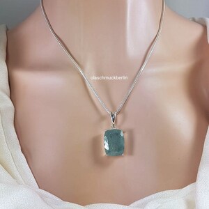 May include: A silver chain necklace with a large, rectangular, green gemstone pendant. The pendant is set in silver and has a faceted design. The text "olaschmuckberlin" is visible on the chain.