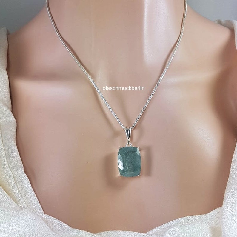 May include: A silver chain necklace with a large, rectangular, green gemstone pendant. The pendant is set in silver and has a faceted design. The text "olaschmuckberlin" is visible on the chain.