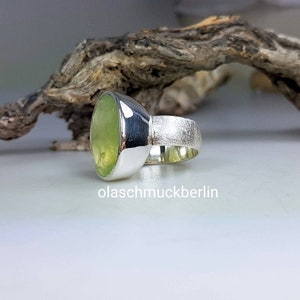May include: A silver ring with a large, oval-shaped green gemstone set in a bezel setting. The ring band is textured and has a hammered finish.