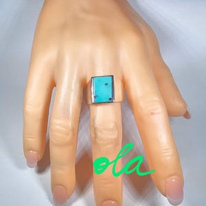May include: A silver ring with a rectangular turquoise stone set in the center. The ring is on a model's finger.