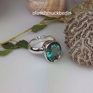 May include: A silver ring with a large, oval-shaped, green gemstone. The ring is set on a white background.