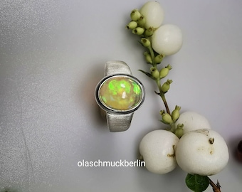 May include: A silver ring featuring a green and white opal gemstone. The ring is set in a brushed silver band.