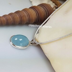 May include: A silver chain necklace with a light blue oval pendant. The pendant is set in silver and has a smooth, polished finish. The chain is a delicate, snake chain style.