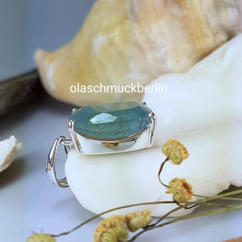 May include: A silver pendant with a light blue aquamarine gemstone. The pendant is oval shaped and has a smooth, polished finish. The gemstone is set in a silver bezel.