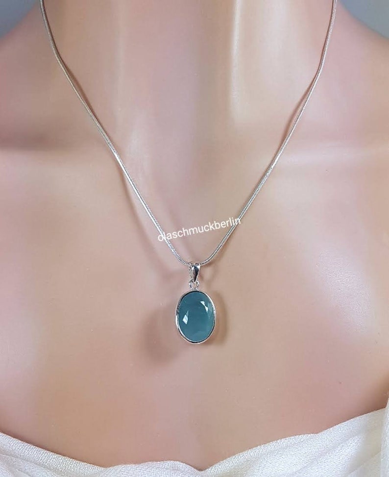 May include: A silver chain necklace with a light blue oval pendant. The pendant is set in silver and has a smooth, polished finish.