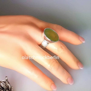 May include: A silver ring with a large, oval-shaped green gemstone. The ring is set on a textured band.