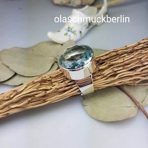 May include: A silver ring with a large, oval-shaped aquamarine gemstone. The ring is set on a wooden surface.