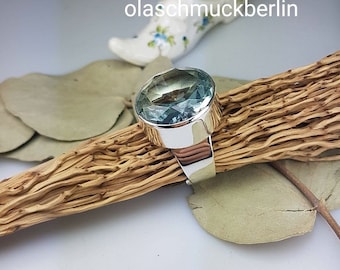 Op de afbeelding: Een zilveren ring met een grote, ovale aquamarijn edelsteen. De ring ligt op een houten oppervlak.