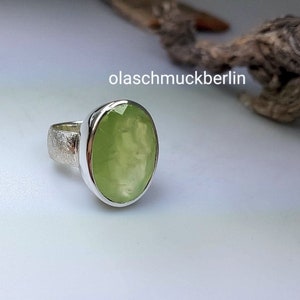 May include: A silver ring with a light green oval gemstone. The ring has a textured band.