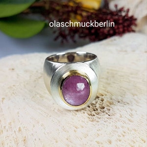 May include: A silver ring with a pink gemstone set in a gold bezel. The ring has a wide band with a textured surface.