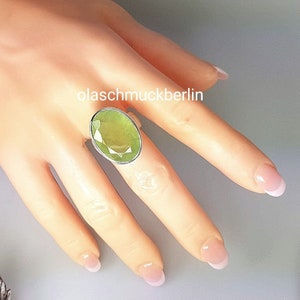 May include: A silver ring with a large, oval-shaped green gemstone. The ring is on a model's finger.