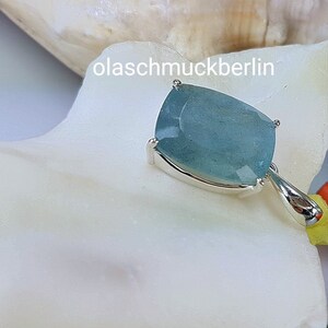 May include: A silver pendant with a light blue aquamarine gemstone. The gemstone is a cushion cut and has a faceted finish. The pendant is on a white background.