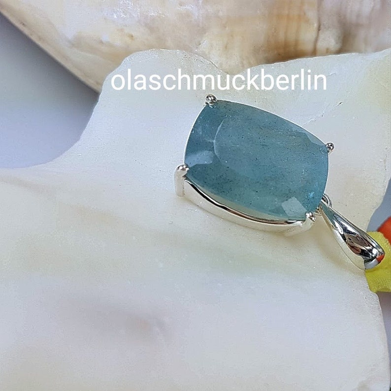 May include: A silver pendant with a light blue aquamarine gemstone. The gemstone is a cushion cut and has a faceted finish. The pendant is on a white background.