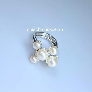 May include: A silver ring with five white pearls set in a cluster design. The ring is made of multiple bands of silver.