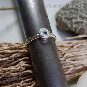 May include: A silver ring with a light blue oval gemstone. The ring is on a gray metal surface.