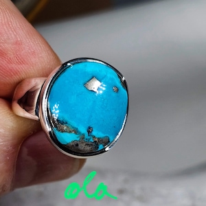 May include: A silver ring with a turquoise stone set in a bezel setting. The turquoise is a vibrant blue with brown and black matrix.