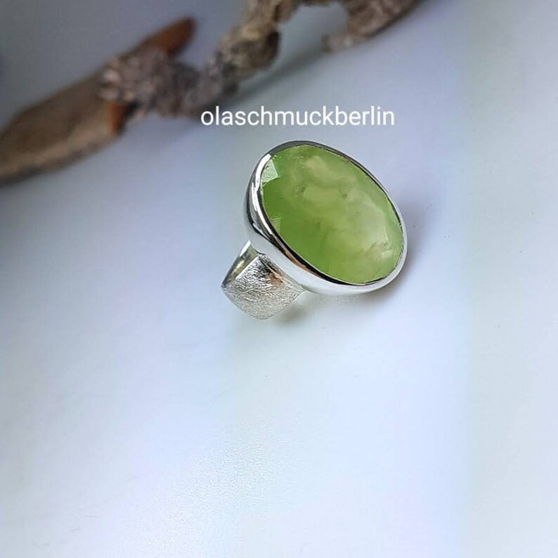 May include: A silver ring with a large, oval-shaped green gemstone. The ring is set in a simple, modern style.