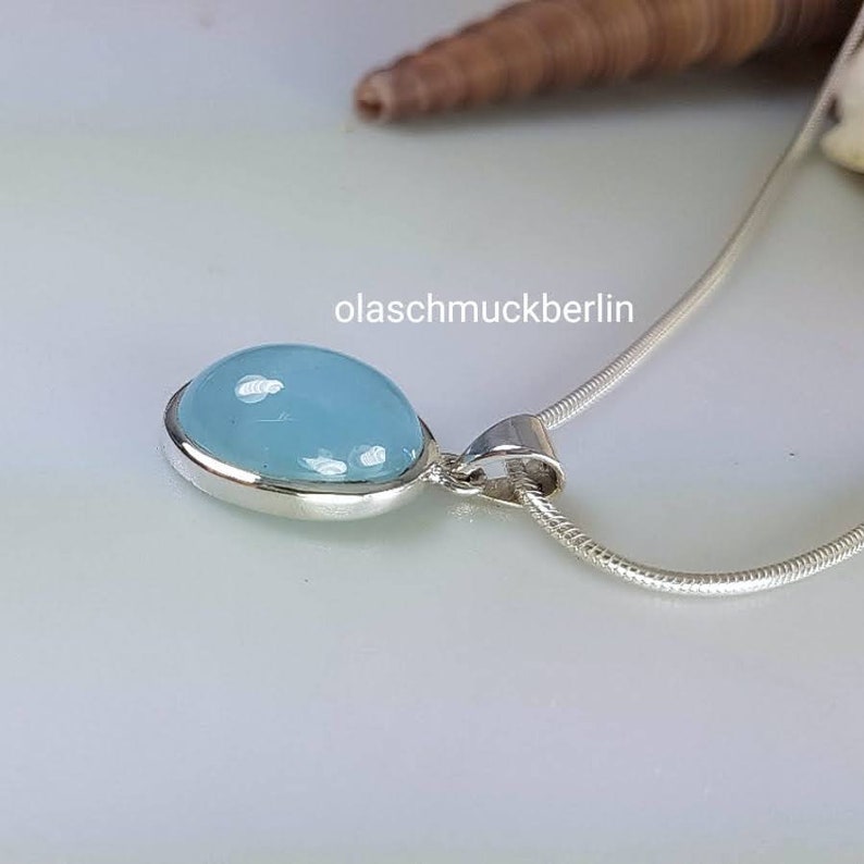 May include: A silver chain necklace with a pendant featuring a light blue oval gemstone.