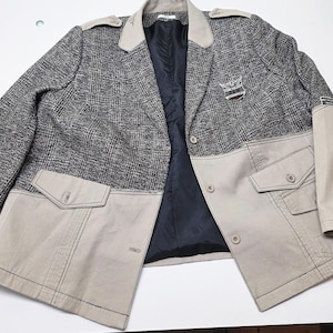 Peut inclure: Un blazer à carreaux gris et noir avec des détails beiges. Le blazer présente des poches, des revers et des épaulettes beiges. Un emblème argenté est sur la poitrine. L'intérieur est noir. Fermeture à deux boutons.