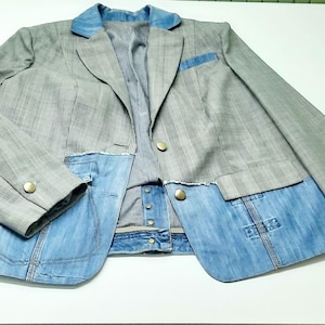 Peut inclure: Un blazer gris avec un col, une poche et une partie inférieure en denim bleu. Le blazer présente un motif à rayures sur les manches et le haut du corps, avec des boutons dorés. La doublure intérieure est en tissu rayé.