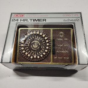 May include: A KMC 24 HR. TIMER in its original packaging. The device features a brown face with a circular dial containing white tabs for time settings, marked with morning, noon, evening, and midnight. A side panel includes switches for Outlet ON, Outlet OFF, and AUTOMATIC settings.