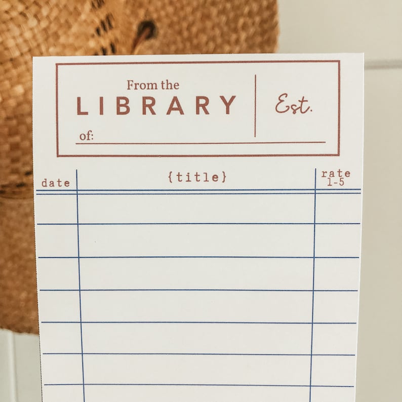May include: A white library card with a brown border and text. The text reads "From the LIBRARY Est." and "of:" above lines for writing. Below are blue horizontal lines for writing, with the words "date", "{title}", and "rate 1-5".