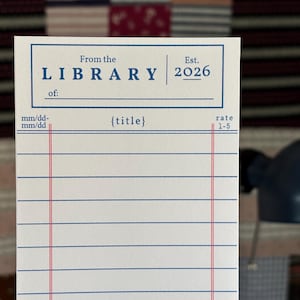 Peut inclure: Une carte de bibliothèque blanche avec des lignes bleues et rouges. La carte porte le texte "From the LIBRARY Est. 2026" en haut, avec des espaces pour "of:" et "{title}". Elle comprend également une section pour une note de 1 à 5.