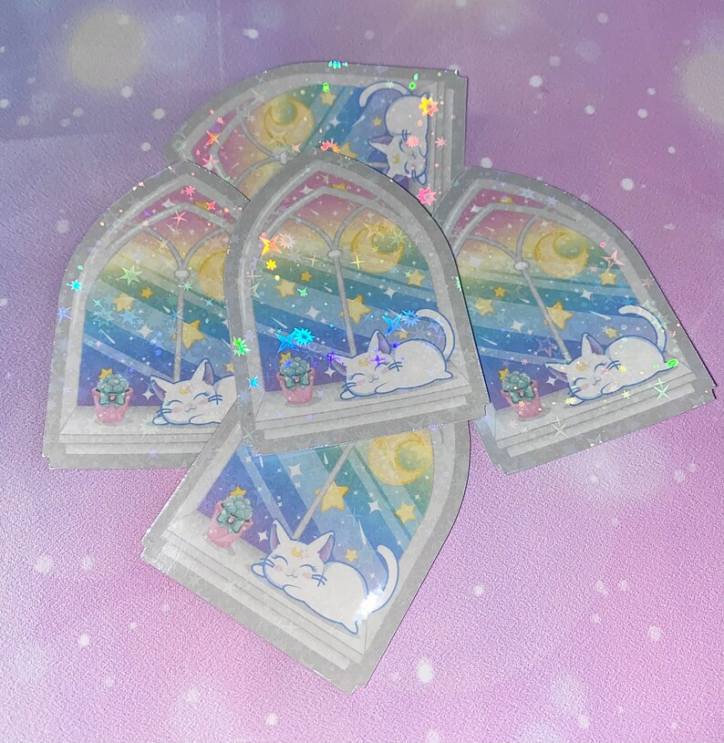 May include: Five iridescent stickers featuring a white cat sleeping in a window with a crescent moon, stars, and a potted plant. The stickers have a holographic finish.