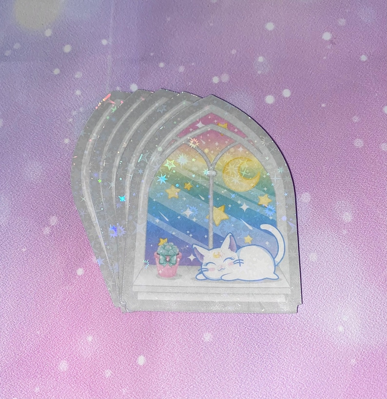 May include: A stack of four iridescent stickers featuring a white cat sleeping in a window with a rainbow and stars. The window is framed in gray and has a crescent moon in the top right corner.