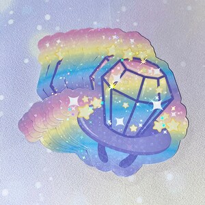 May include: A stack of rainbow holographic stickers featuring a cartoon diamond with a ring around it. The diamond is surrounded by stars and sparkles.