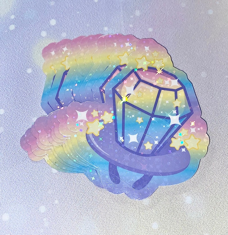 May include: A stack of rainbow holographic stickers featuring a cartoon diamond with a ring around it. The diamond is surrounded by stars and sparkles.