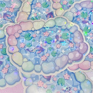 Puede incluir: Un conjunto de pegatinas iridiscentes con un dise&ntilde;o caprichoso de peces koi nadando en un estanque rodeado de rocas y nen&uacute;fares de colores pastel. Las pegatinas tienen un acabado hologr&aacute;fico que brilla a la luz.